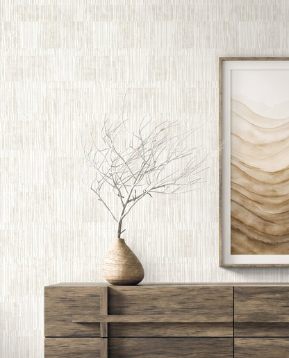 A wooden dresser with a vase and art sits before Abstract Vertical Stripes Wallpaper in textured beige tones.