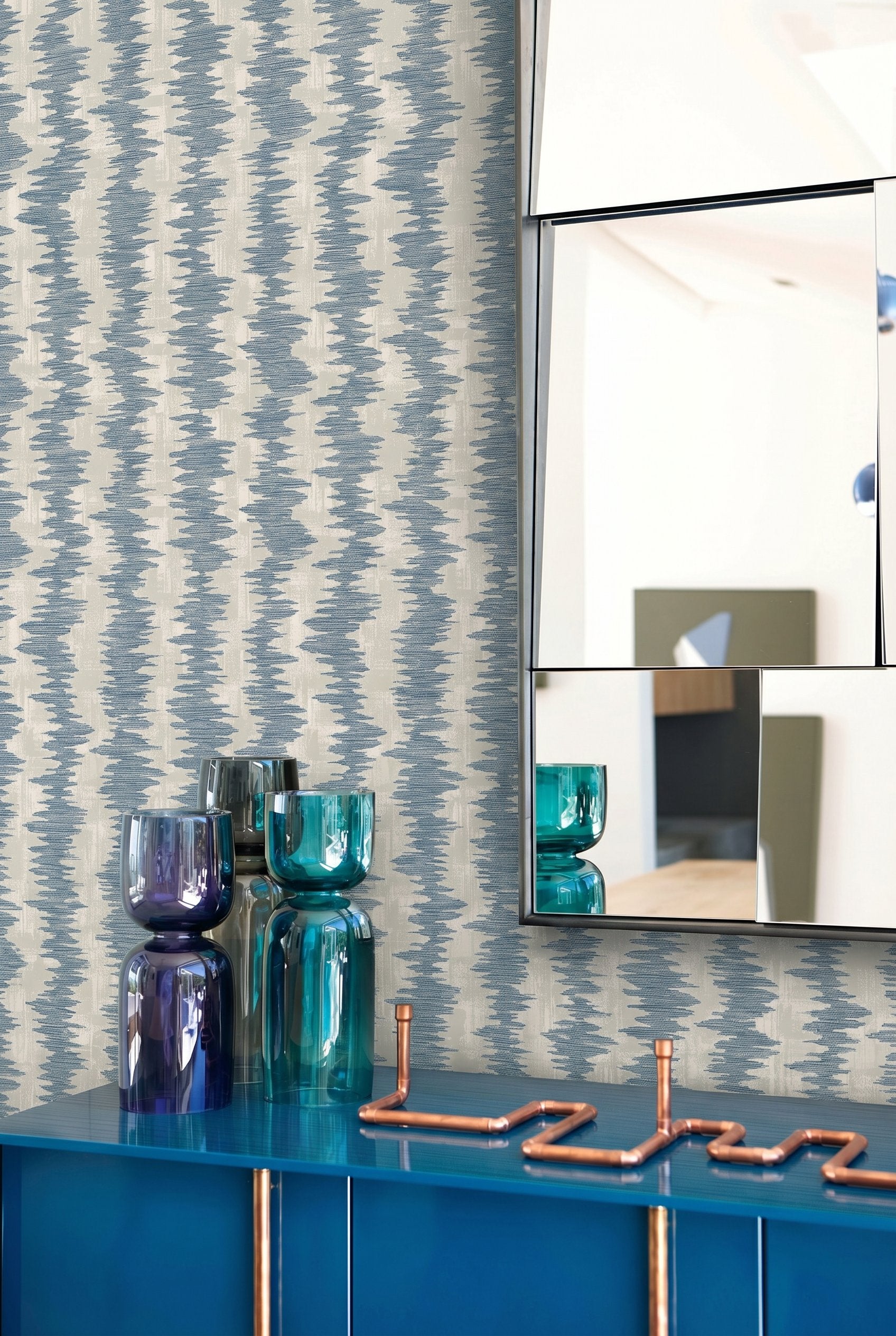 Ikat Stripe Wallpaper, mirrored wall art, glass vases, and a blue cabinet topped with copper pipe decor.