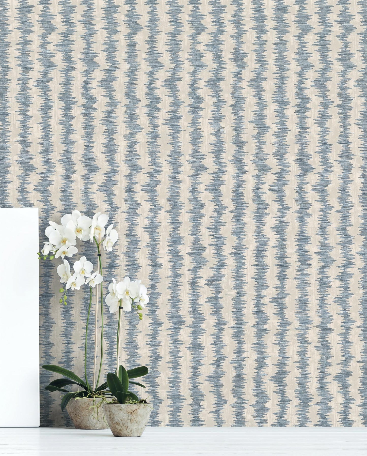 Two potted orchids on a white floor in front of beige and blue Ikat Stripe Wallpaper.