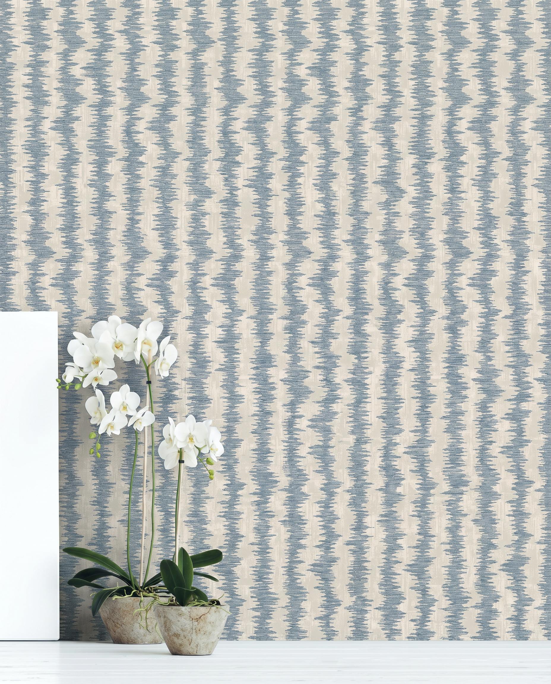 Two potted orchids on a white floor in front of beige and blue Ikat Stripe Wallpaper.