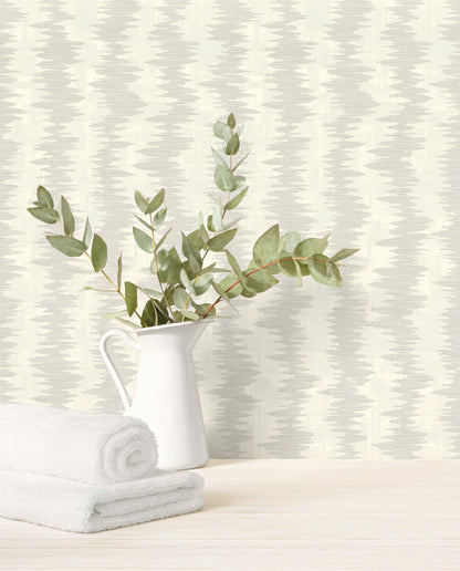White pitcher with leafy branches and towels on wood, set against Ikat Stripe Wallpaper in the background.