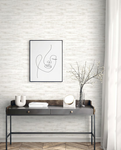 Modern console table with minimalist decor, a vase, abstract face art, and Stone Nebulite Wallpaper on a light brick wall.