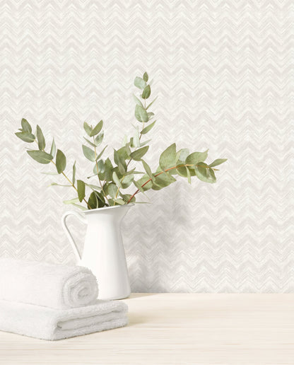 White pitcher with eucalyptus branches and towels on wood surface, set against Chevron Wallpaper in white/off white.