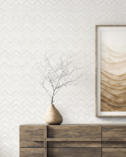 A minimalist wooden sideboard with a bare branch and abstract art on cream Chevron Wallpaper.