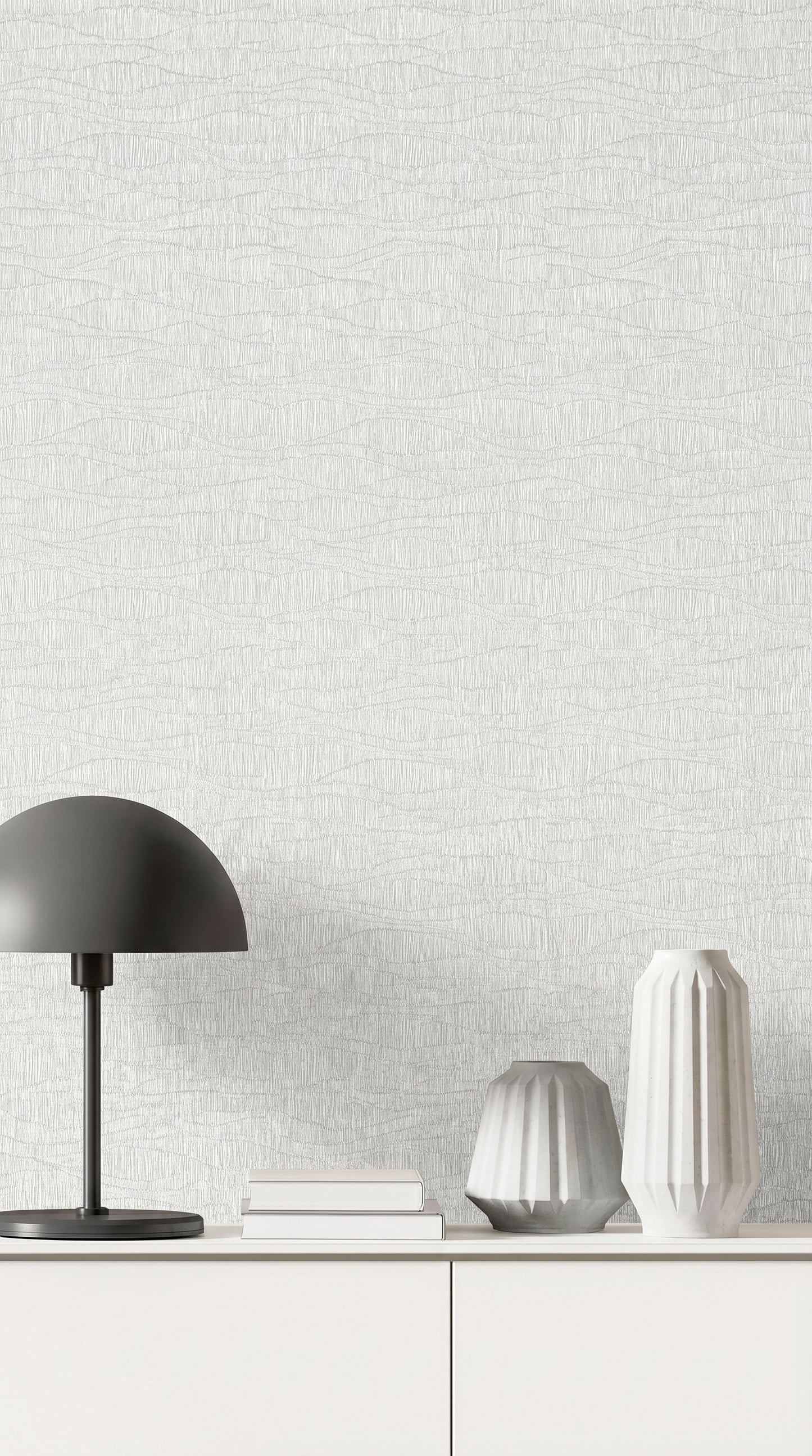 A minimalist white sideboard with vases, a black lamp, and books set against Wavy Wallpaper.