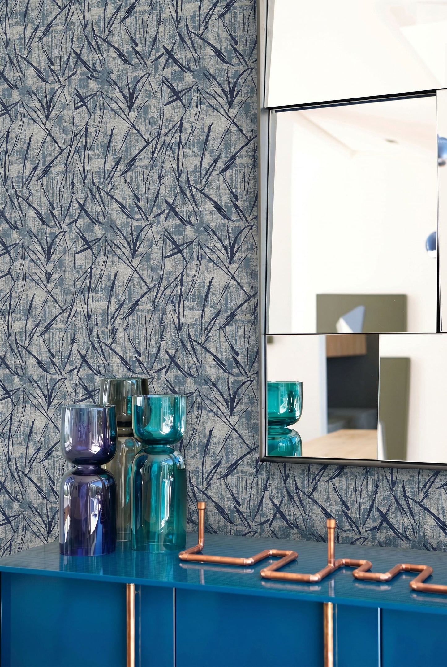 Brushstroke Wallpaper, stacked glass vases, geometric mirrors, and copper pipe art on a modern sideboard.