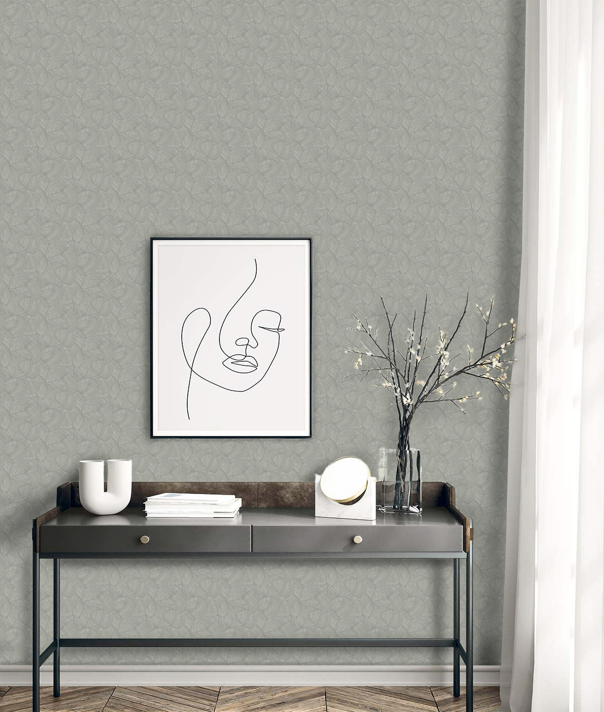 Minimalist desk with decor, framed line art, and vase in front of Fan Wallpaper and sheer curtain.