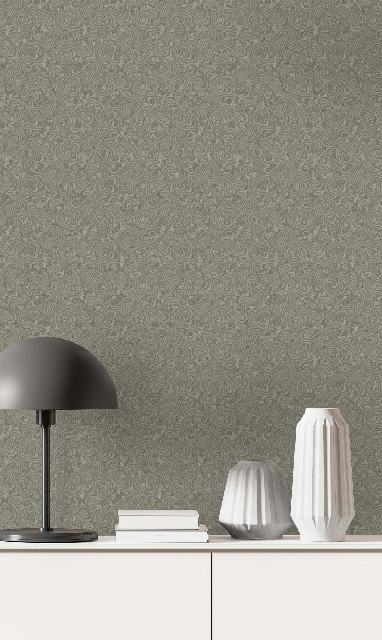 A black lamp, two white vases, and books rest on a white cabinet against Fan Wallpaper in textured green.