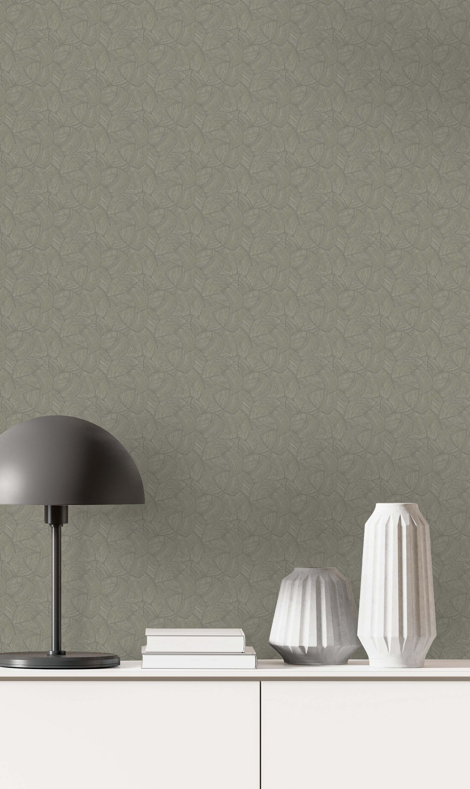 A black lamp, two white vases, and books rest on a white cabinet against Fan Wallpaper in textured green.