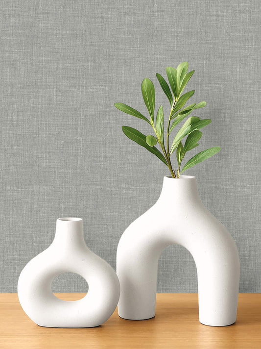 Two modern white ceramic vases on wood, set against textured gray Faux Linen Wallpaper.