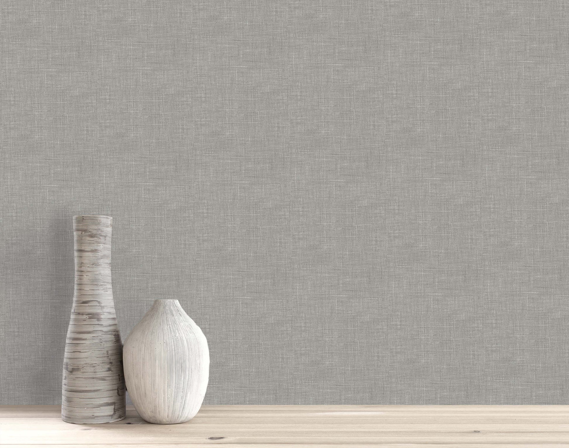 Two neutral-toned ceramic vases on light wood set against a gray Faux Linen Wallpaper wall.