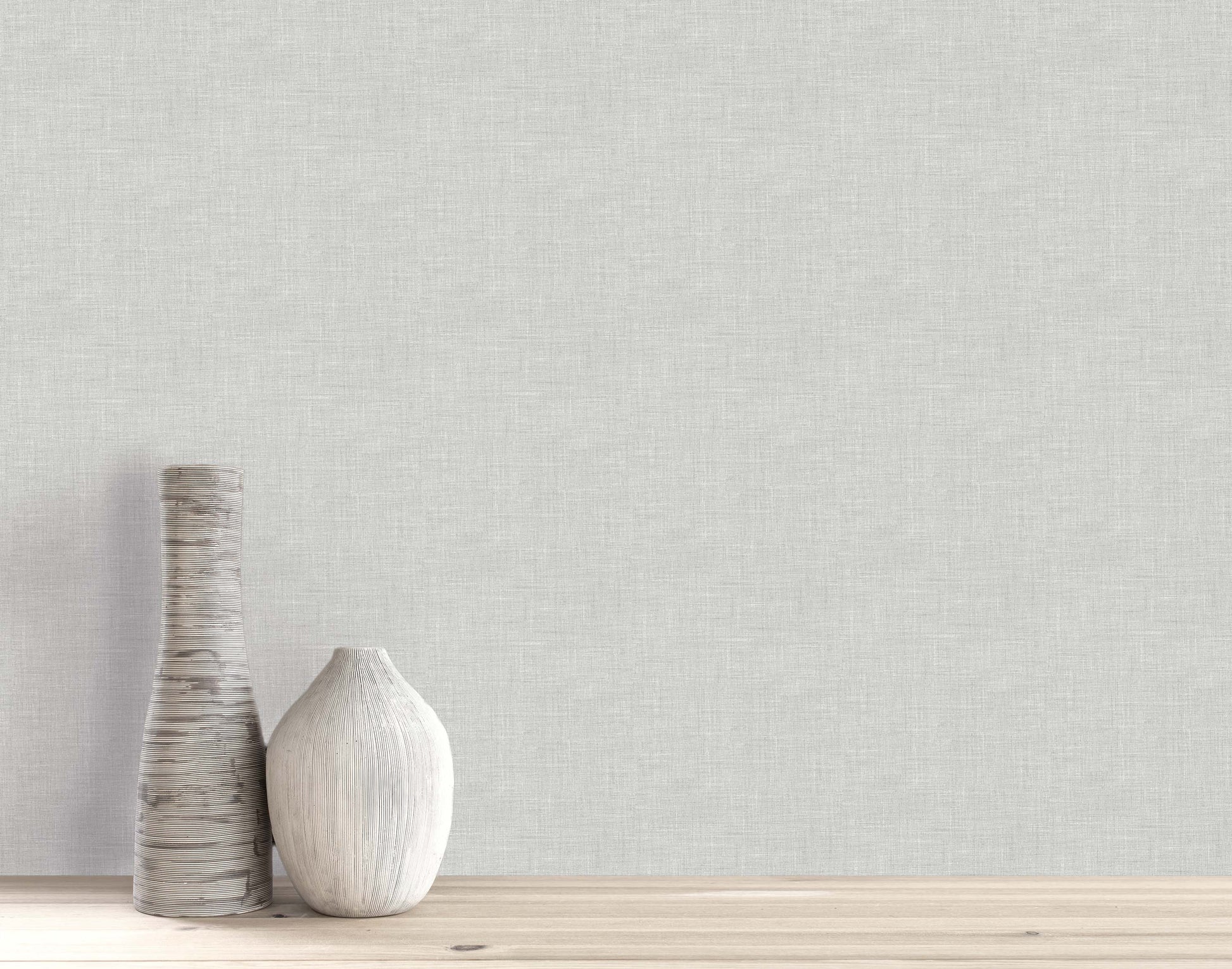 Two vases on a wooden surface with textured light gray Faux Linen Wallpaper as a washable backdrop.