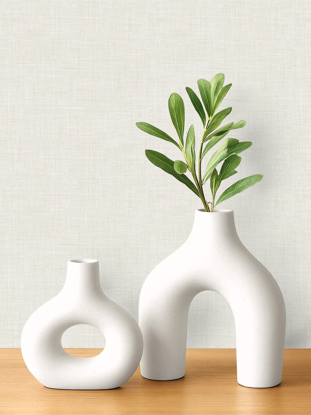 Two modern white ceramic vases on wood, set against a light Faux Linen Wallpaper background.