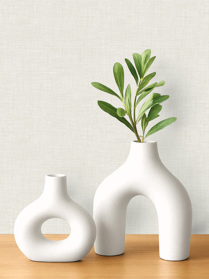 Two modern white ceramic vases on wood, set against a light Faux Linen Wallpaper background.