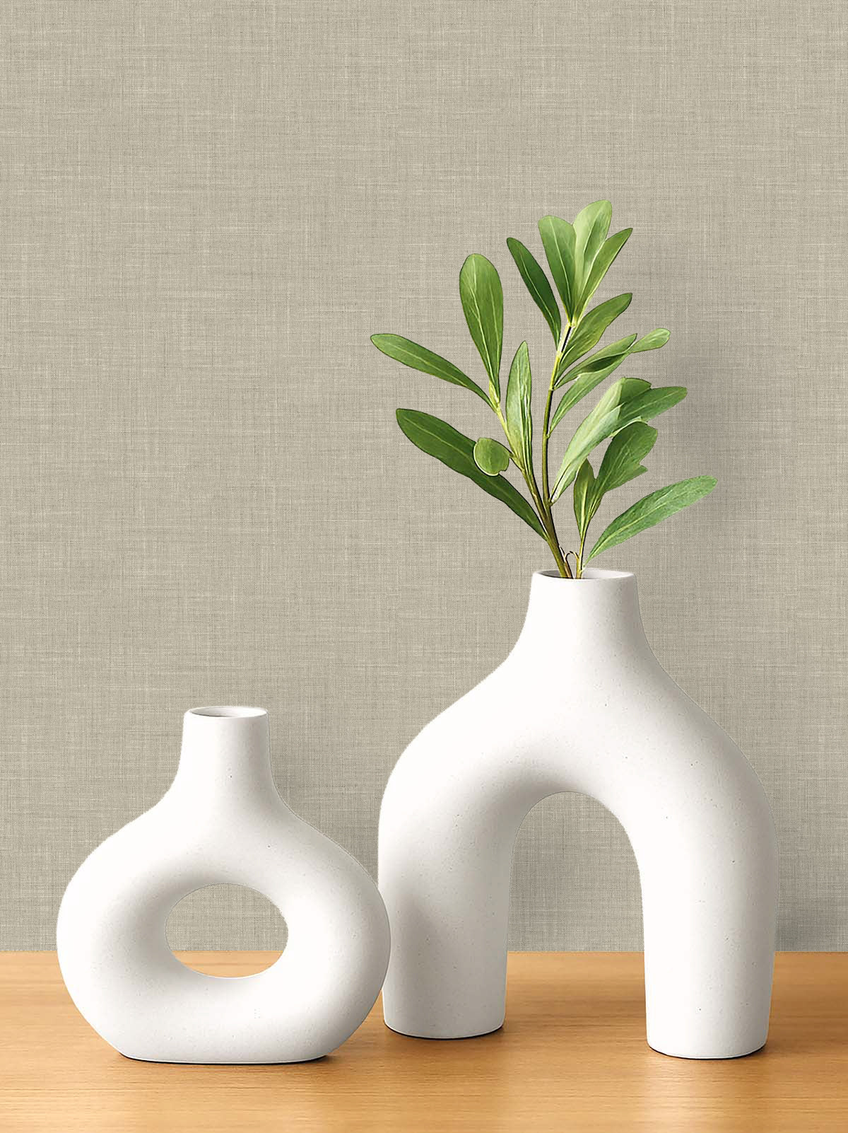 Two white ceramic vases, one with branches, sit on wood against a beige Faux Linen Wallpaper backdrop.