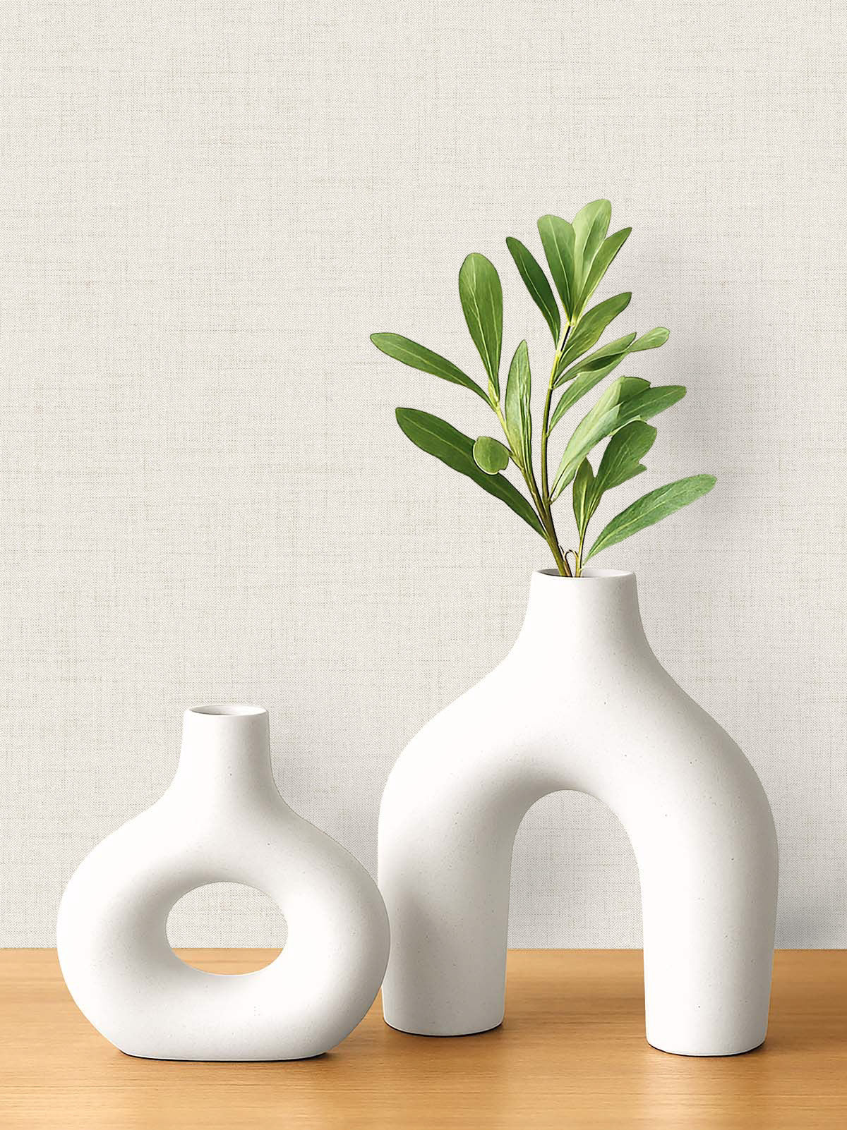 Two modern white ceramic vases on a wooden surface with faux linen wallpaper in the background.
