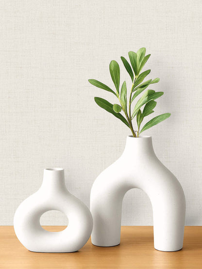 Two modern white ceramic vases on a wooden surface with faux linen wallpaper in the background.