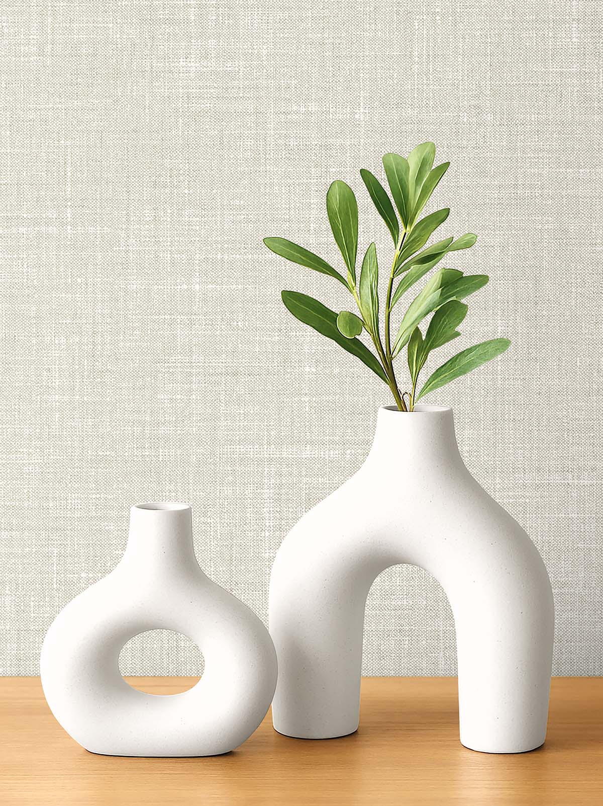 Two white vases with green leaves sit on wood against washable Faux Linen Wallpaper.