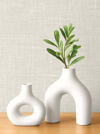 Two white vases with green leaves sit on wood against washable Faux Linen Wallpaper.