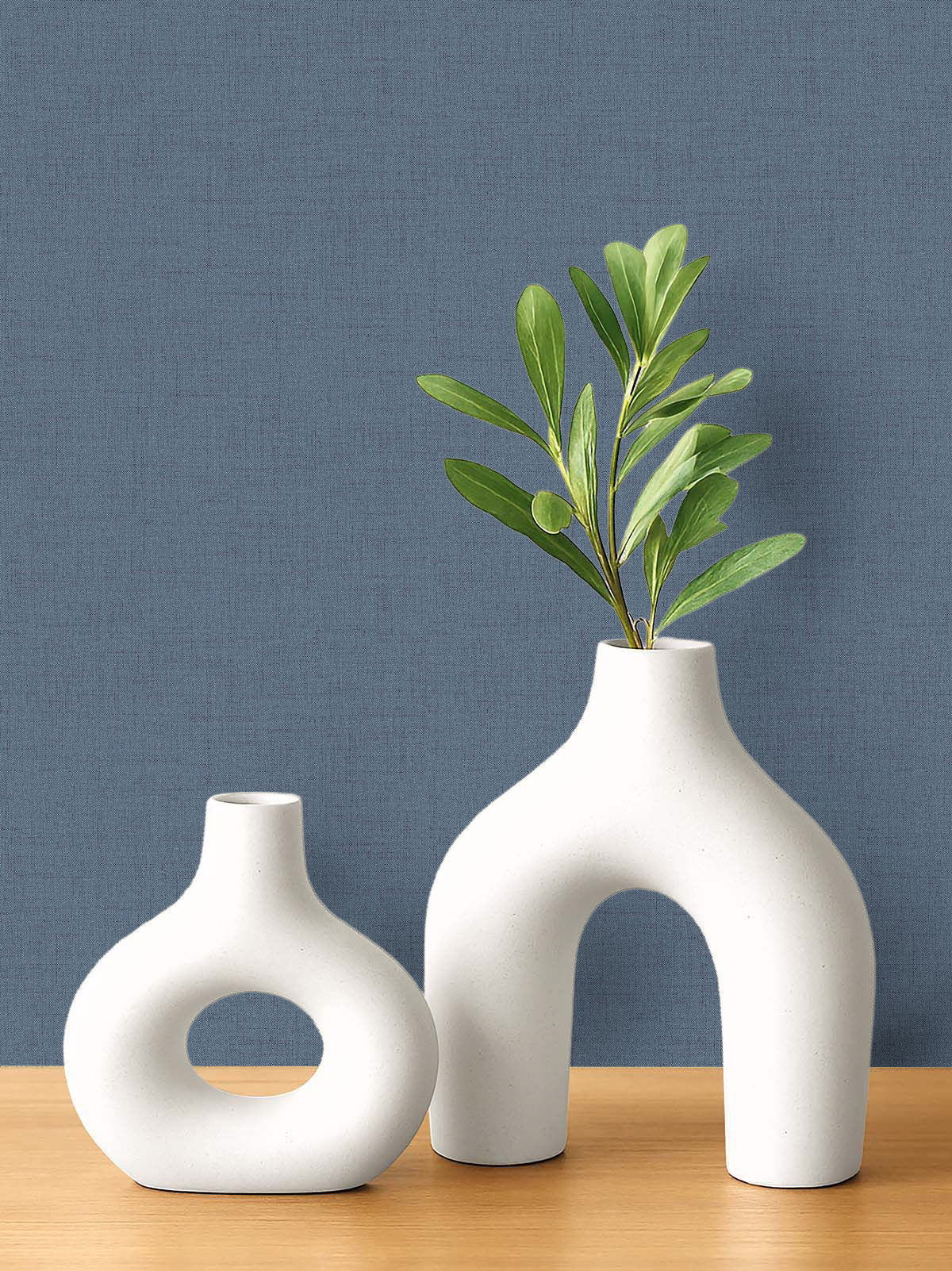 Two modern white ceramic vases on wood, set against blue faux linen wallpaper that's easy to clean.