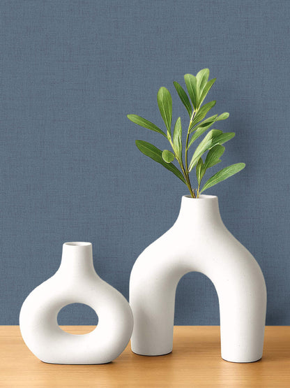 Two modern white ceramic vases on wood, set against blue faux linen wallpaper that's easy to clean.