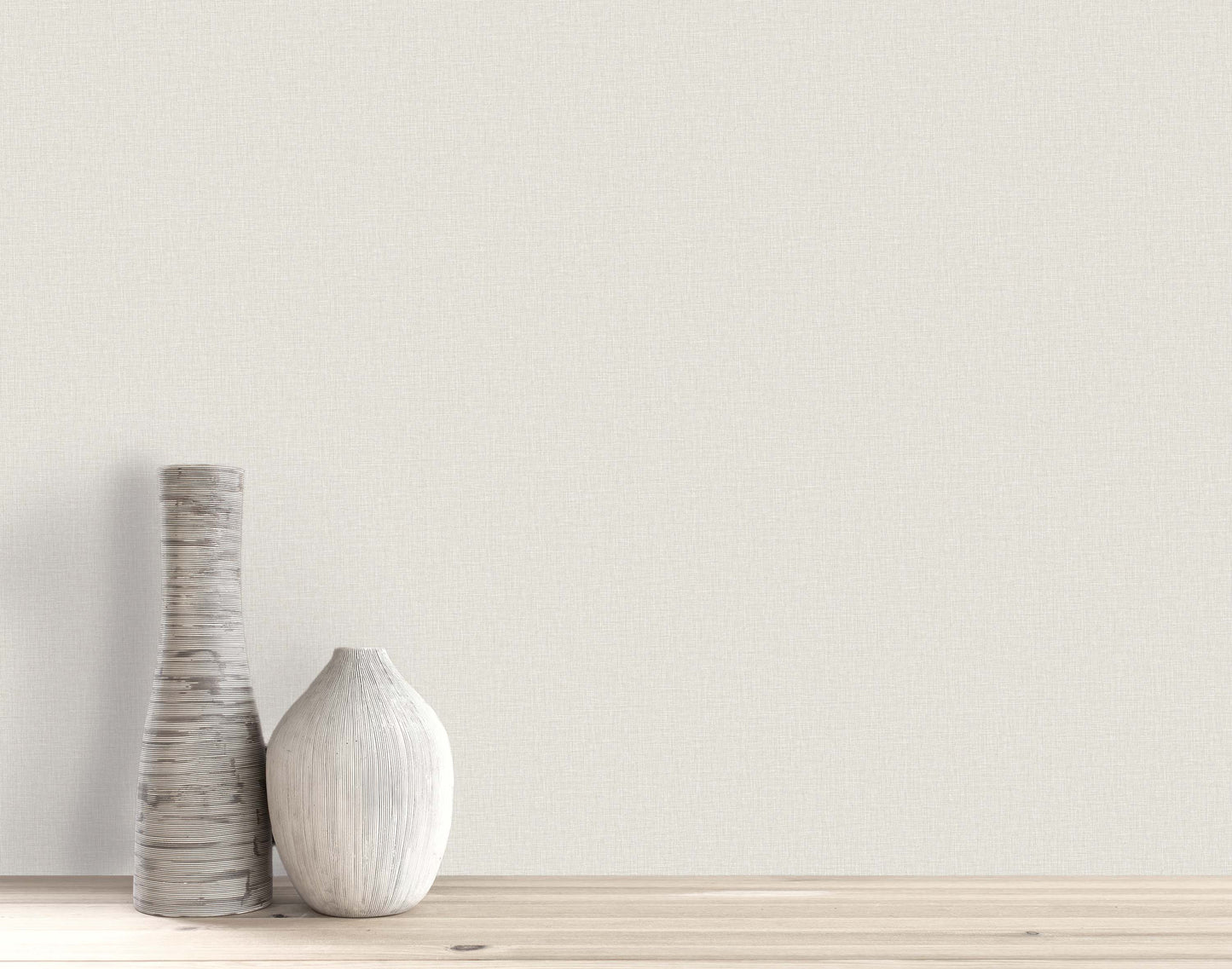 Two textured white vases on a light wooden surface against a Pearly Linen Wallpaper off-white wall.