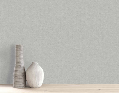 Two decorative vases sit on a wooden surface against a light gray Pearly Linen Wallpaper textured wall.
