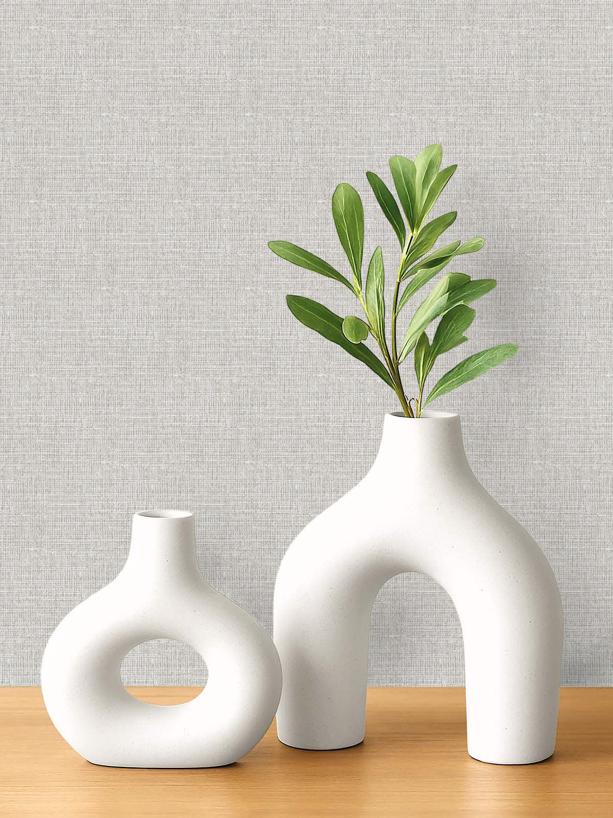 Two white vases on wood, set against Woven Linen Effect Wallpaper in light gray.