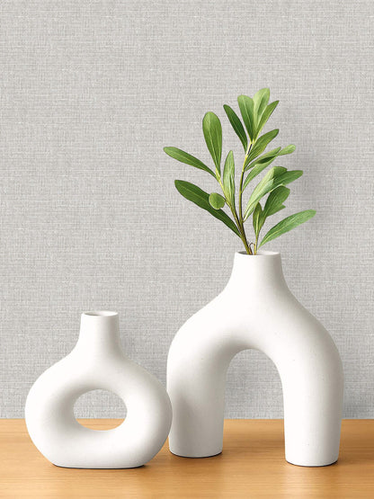 Two white vases on wood, set against Woven Linen Effect Wallpaper in light gray.