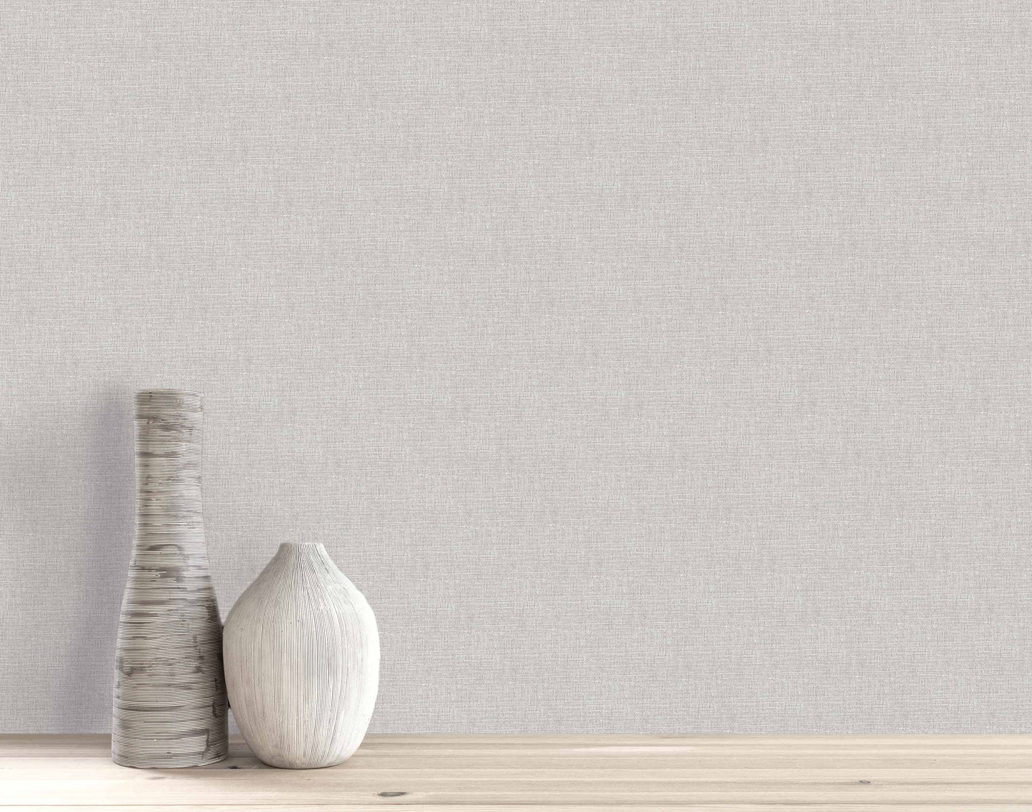 Two textured ceramic vases on a wooden surface with a Woven Linen Effect Wallpaper backdrop in light gray.