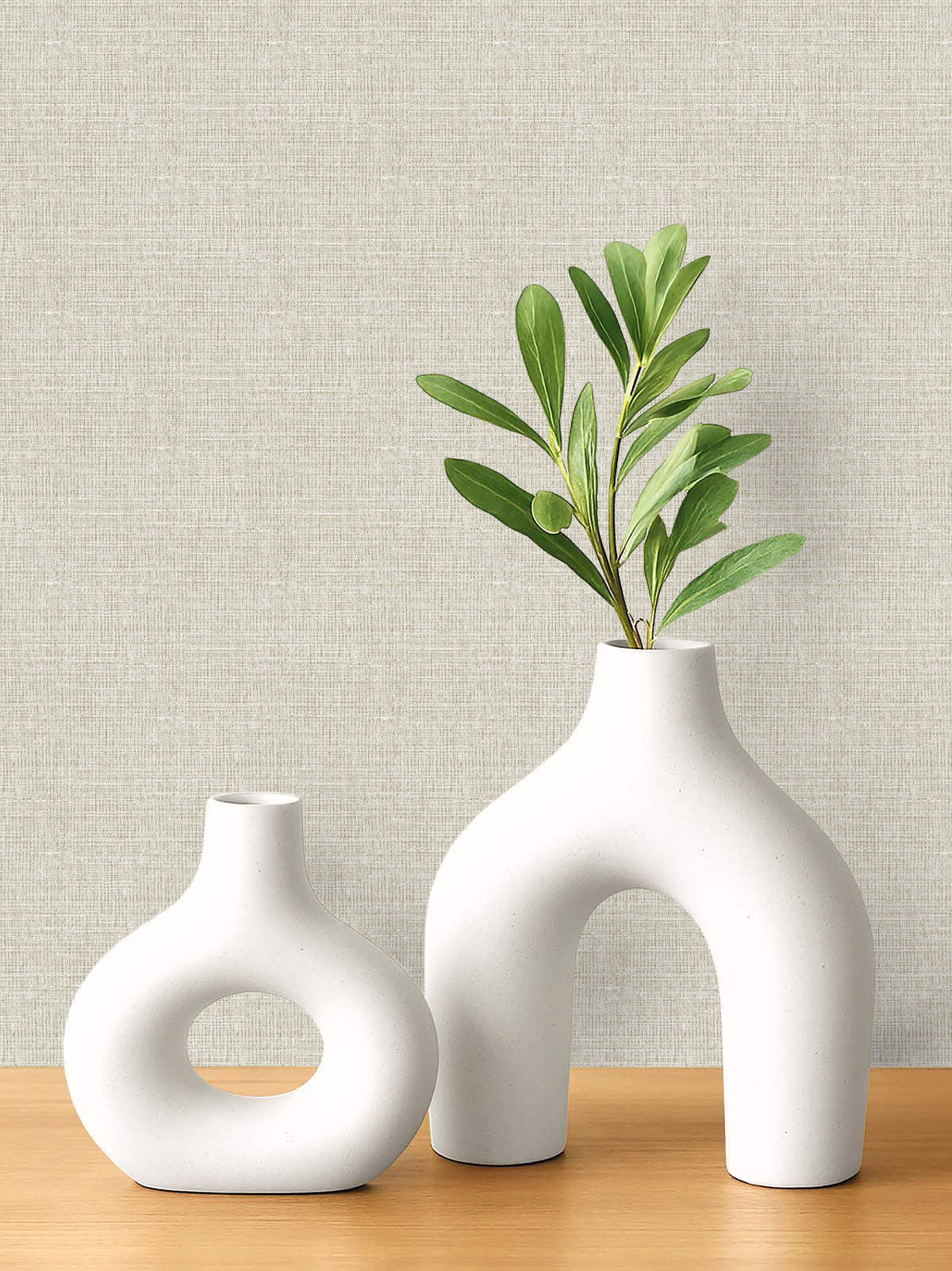Two white ceramic vases on wood, one with green stems, set against Woven Linen Effect Wallpaper.