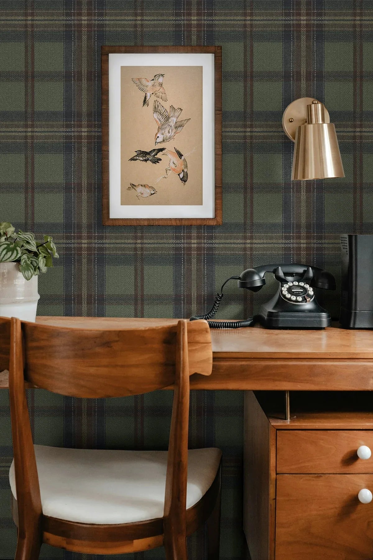 A wooden desk with a rotary phone, lamp, plant, and bird art on Broken Twill Plaid Peel Stick wallpaper.