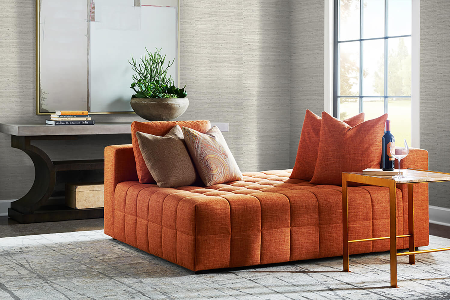 Orange sofa with decorative pillows in a living room setting with a wall decorated Gray Weave Grasscloth Effect Peel & Stick Casa Mia Wallcovering.
