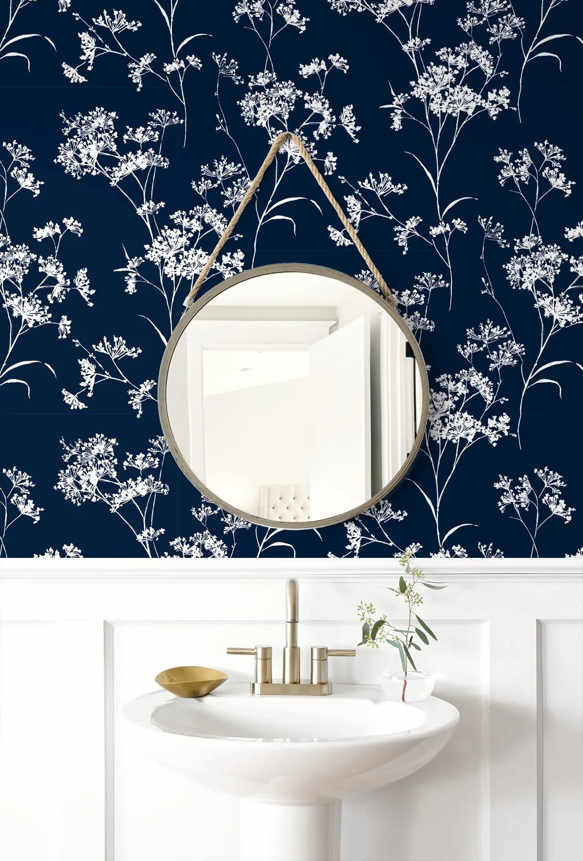 Round mirror above white sink with gold faucet, against Soft Scent Floral Peel Stick wallpaper and white wainscoting.