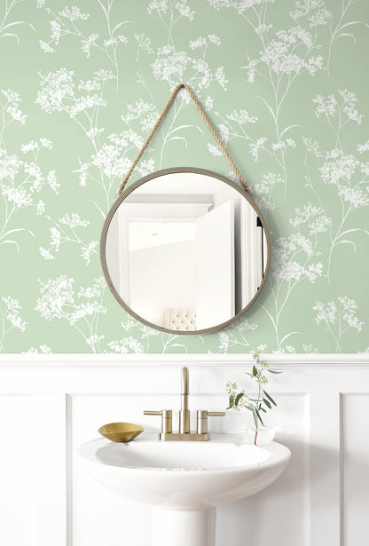 Round mirror hanging on a wall decorated with Green Soft Scent Floral Peel & Stick Casa Mia Wallcovering and a sink below.