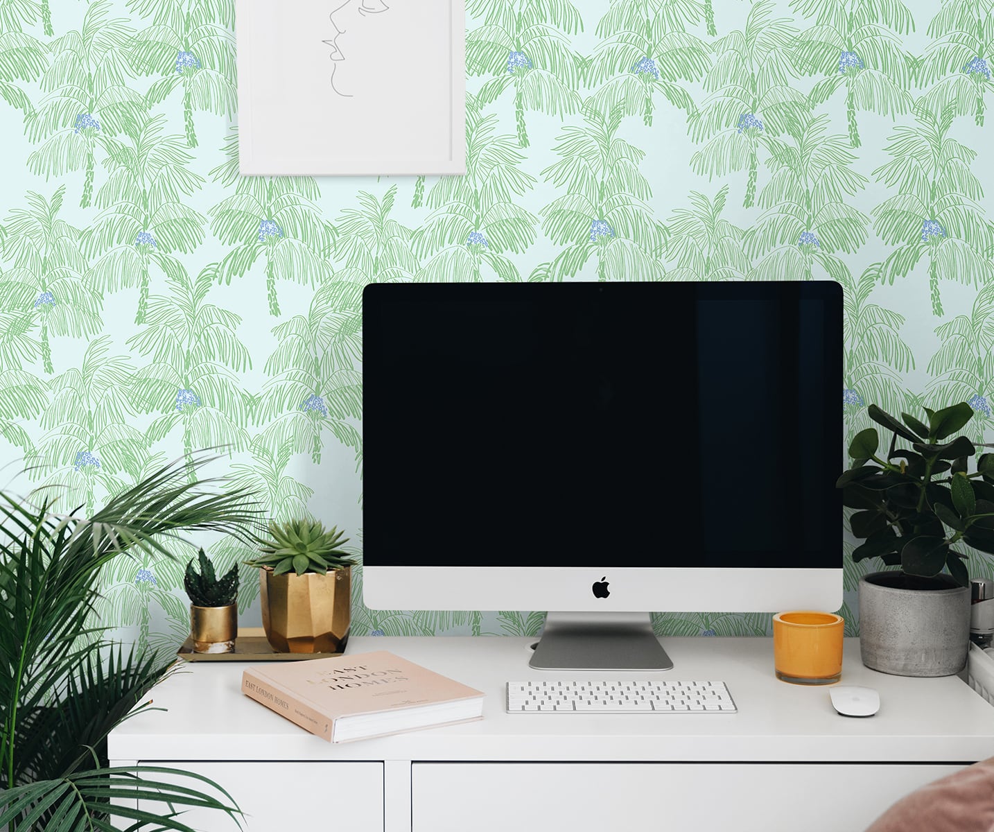 Modern office desk with computer monitor, plants, and decor against a wall decorated with Green Palm Peel & Stick Casa Mia Wallcovering.
