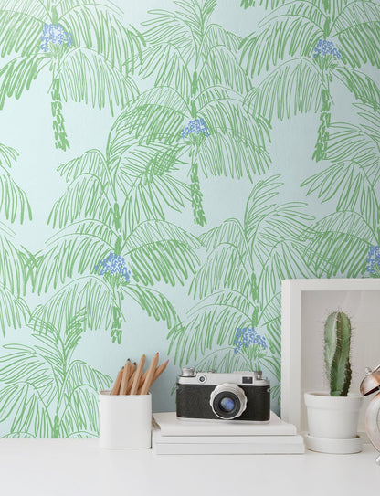 Wall decorated with Green Palm Peel & Stick Casa Mia Wallcovering and desk setup featuring a camera, books, and a cactus.