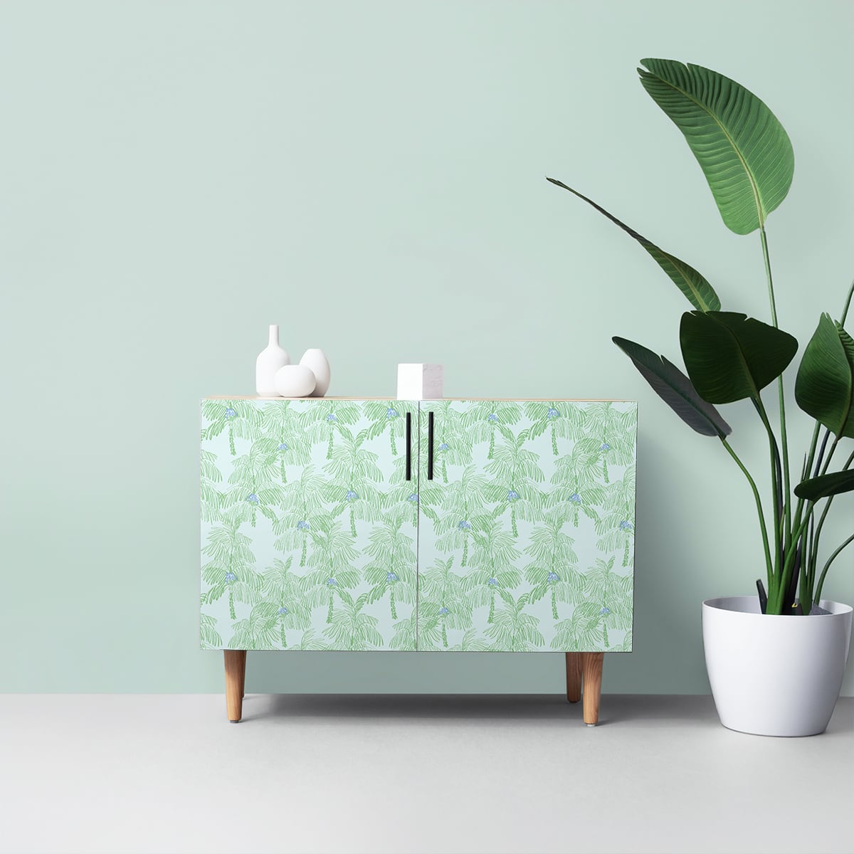 Cabinet with a Green Palm Peel & Stick Casa Mia Wallcovering.
 next to a potted plant on a light green background.