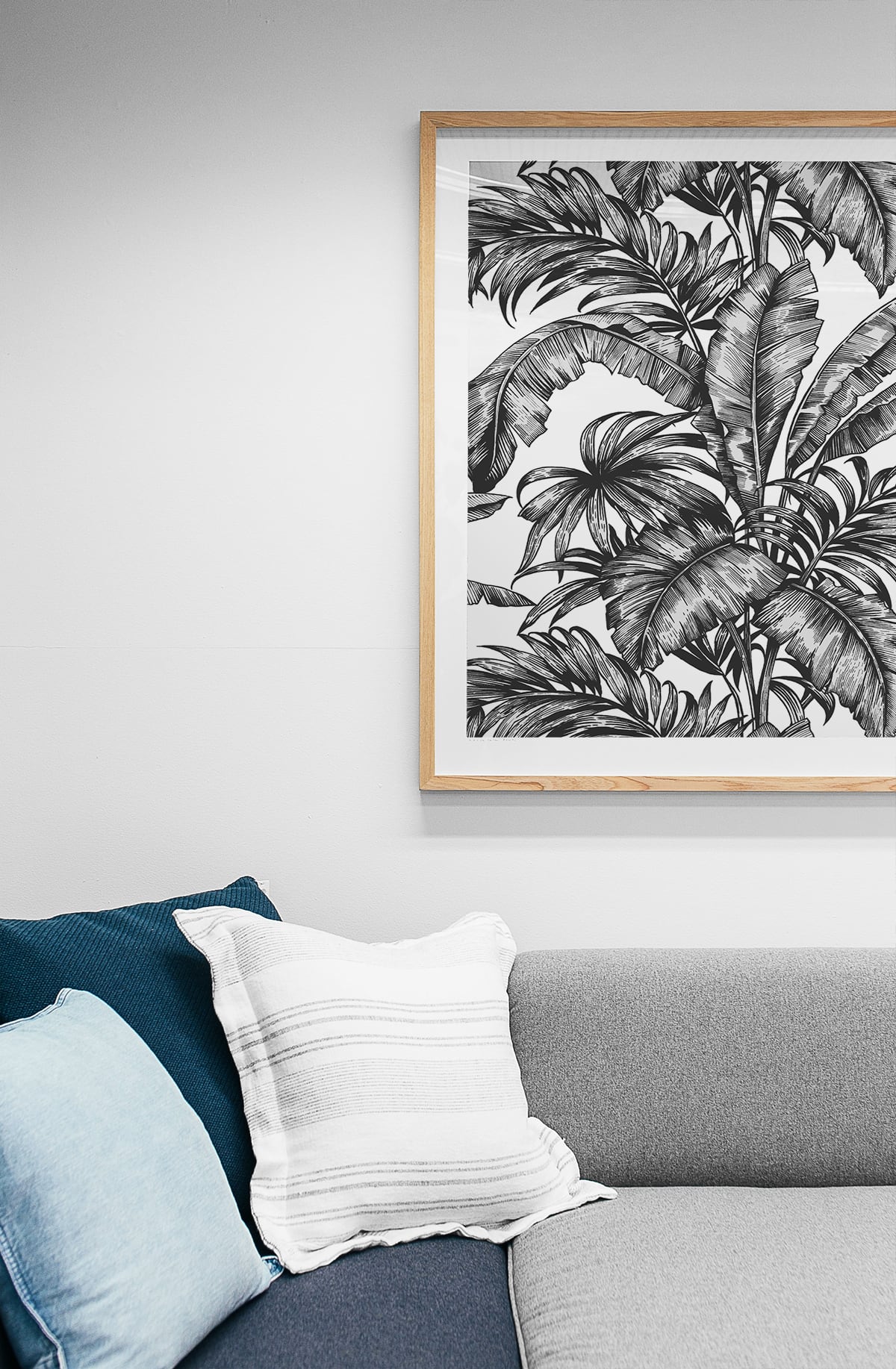 Framed with Black Rainforest Palm Peel & Stick Casa Mia Wallcovering on a wall above a sofa with blue and gray cushions.