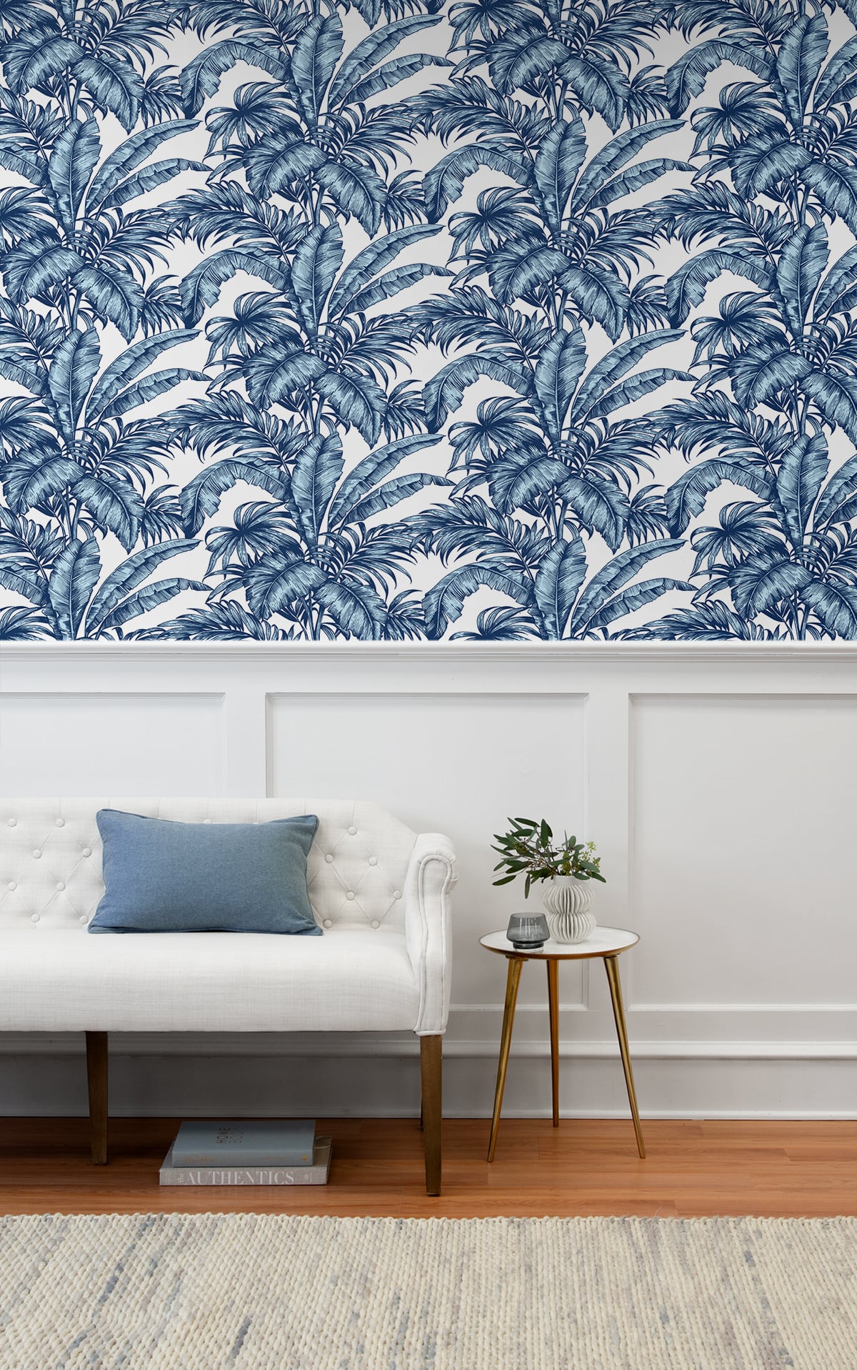 Living room with white sofa, blue pillow, and small table against a wall decorated with Blue Rainforest Palm Peel & Stick Casa Mia Wallcovering.