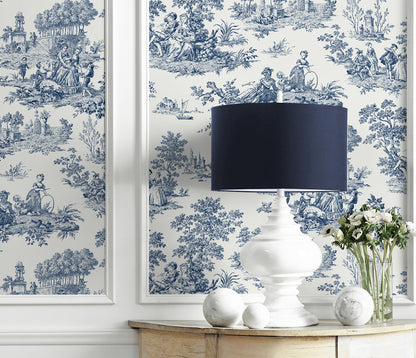 White table with a white lamp, decorative balls, and a vase of flowers against a wall decorated with Blue Toile de Jouy Peel & Stick Casa Mia Wallcovering.
