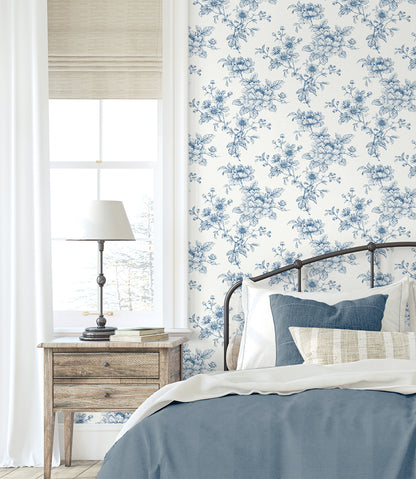 Bedroom wall decorated with Blue Cherished Rose Peel & Stick Casa Mia Wallcovering, wooden nightstand, and bed with blue bedding.