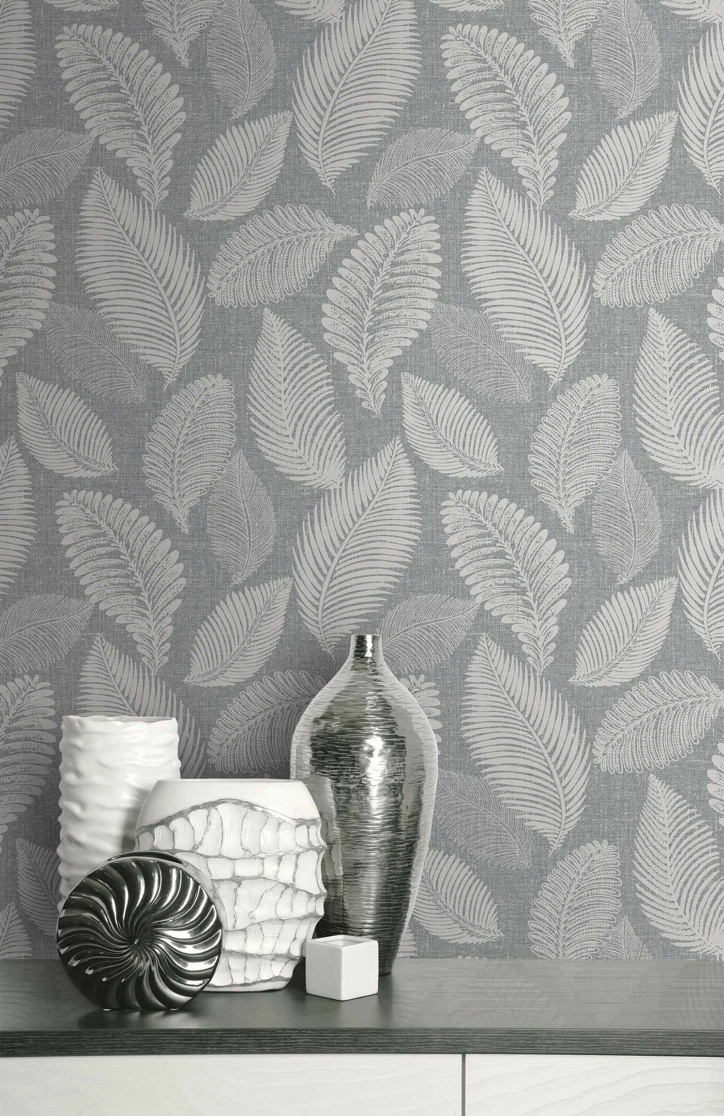 Decorative vases and a bottle on a surface with a wall decorated with Templeton Gray Scattered Leaves Wallpaper.
