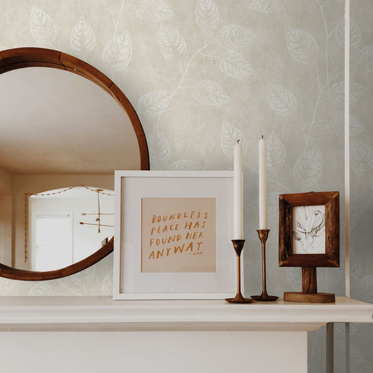 Decorative setup with a mirror, framed text, and candles on a shelf against a wall decorated with Beige Branch Of Leaves Wallpaper.
