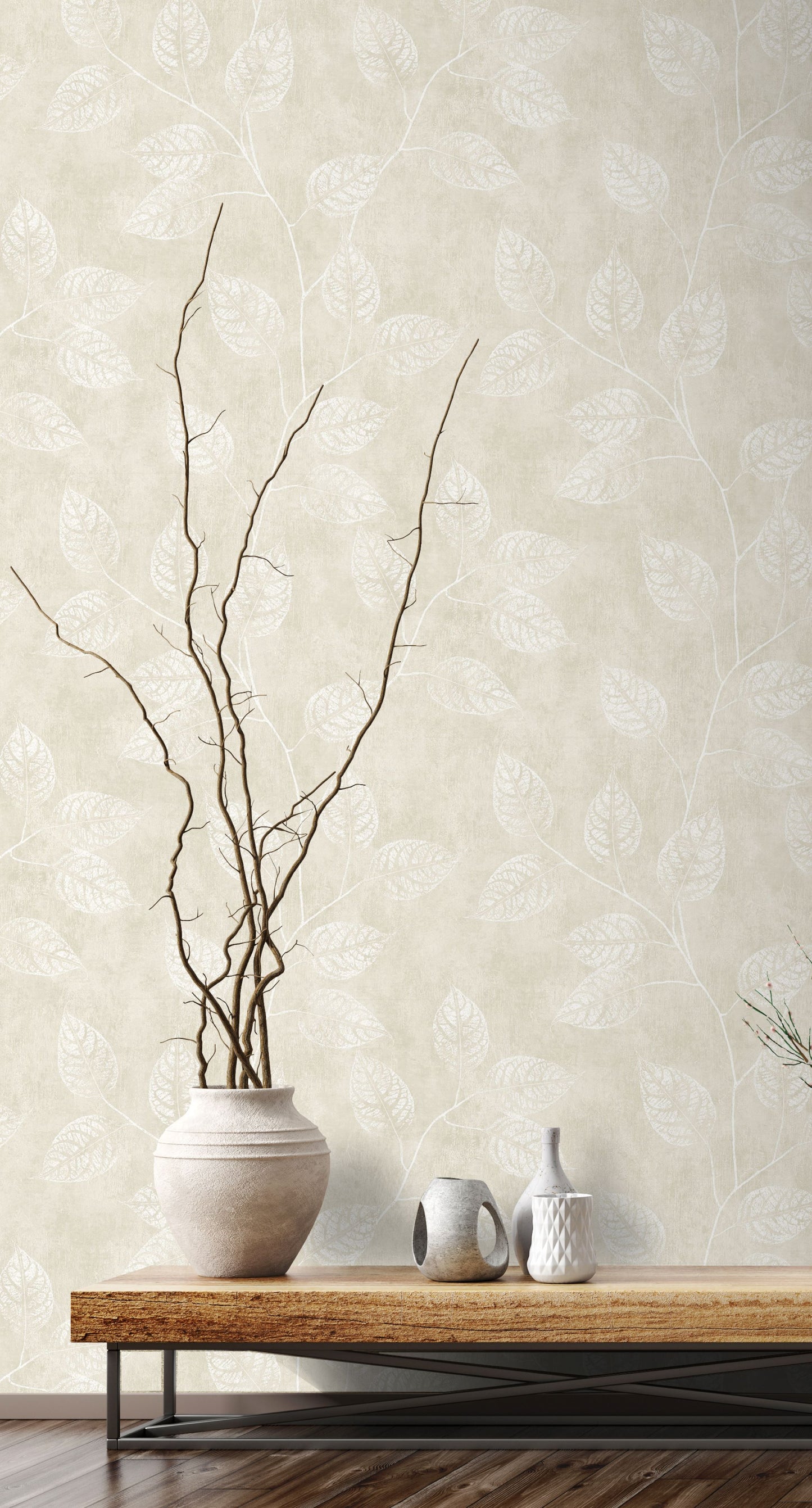 Vase with branches on a wooden table against a wall decorated with Beige Branch Of Leaves Wallpaper.
