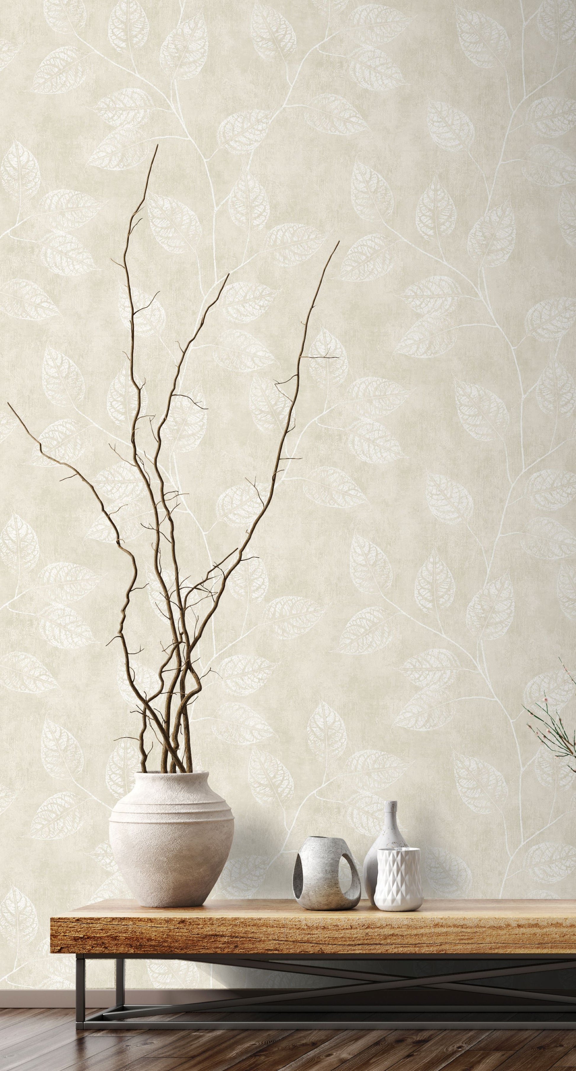 Vase with branches on a wooden table against a wall decorated with Beige Branch Of Leaves Wallpaper.
