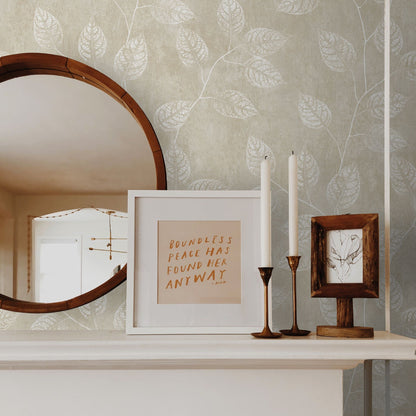 Decorative shelf with a mirror, framed quote, candles, and picture frame against a wall decorated with Sand Yellow & Cream Branch Of Leaves Wallpaper.
