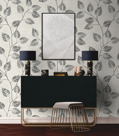 Modern interior design with a black console table, lampshades, and decorative items against a wall decorated with Black & Beige Branch Of Leaves Wallpaper.
