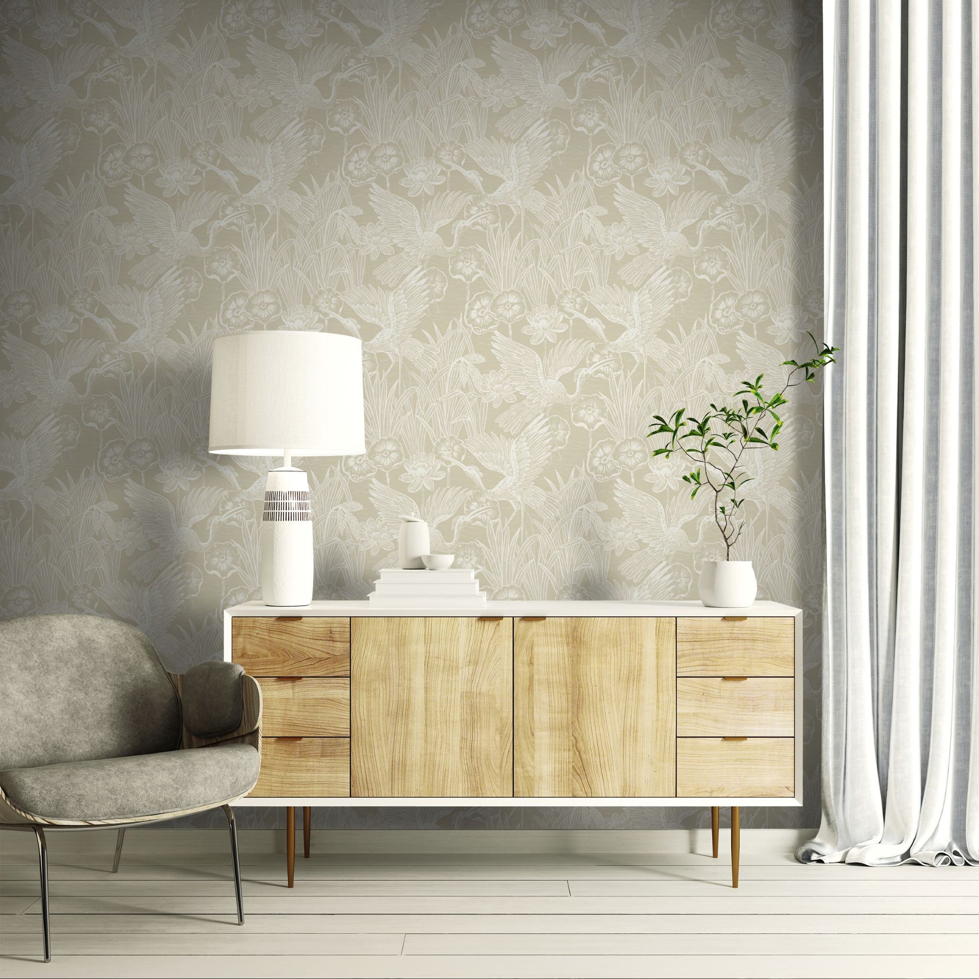 Modern living room with wooden sideboard, gray armchair, and decorative items against a wall decorated with Beige Marsh Heron Wallpaper.

