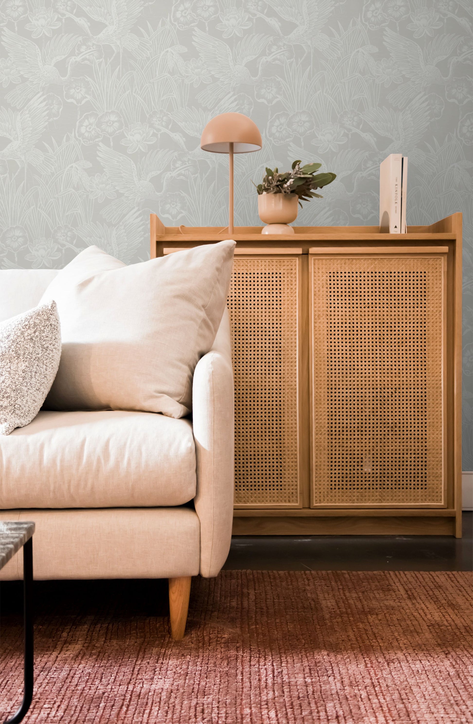 Living room with beige sofa, wooden cabinet, and decorative items against a wall decorated with White/Off White Marsh Heron Wallpaper.
